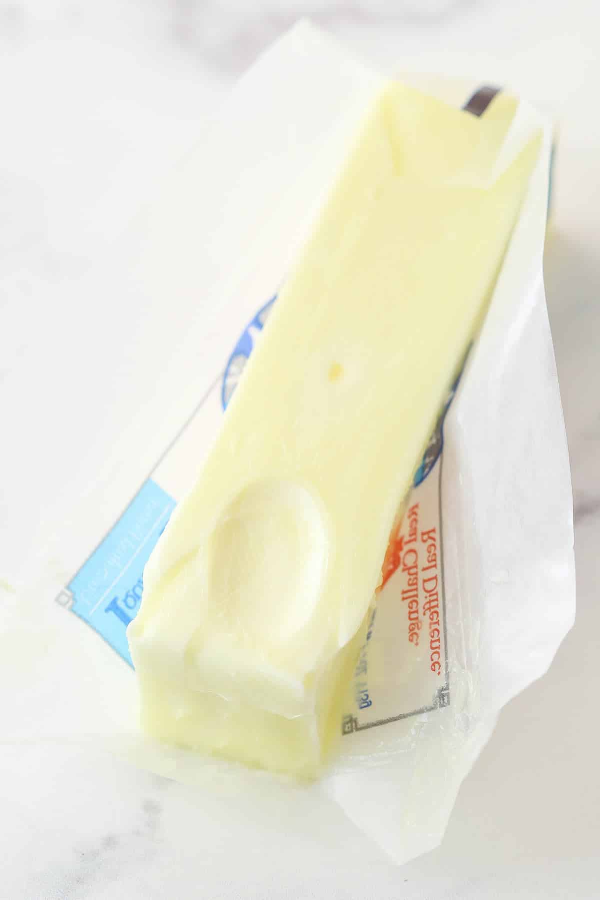 Ready to learn all about how to soften butter? It's a crucial step in many baking recipes that is often overlooked or done incorrectly. Let me walk you through why it's important and 6 different ways to do it. stick of softened butter partially unwrapped on marble background with a fingerprint