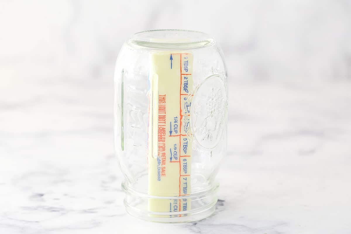 a stick of butter standing up under a mason jar on a marble background
