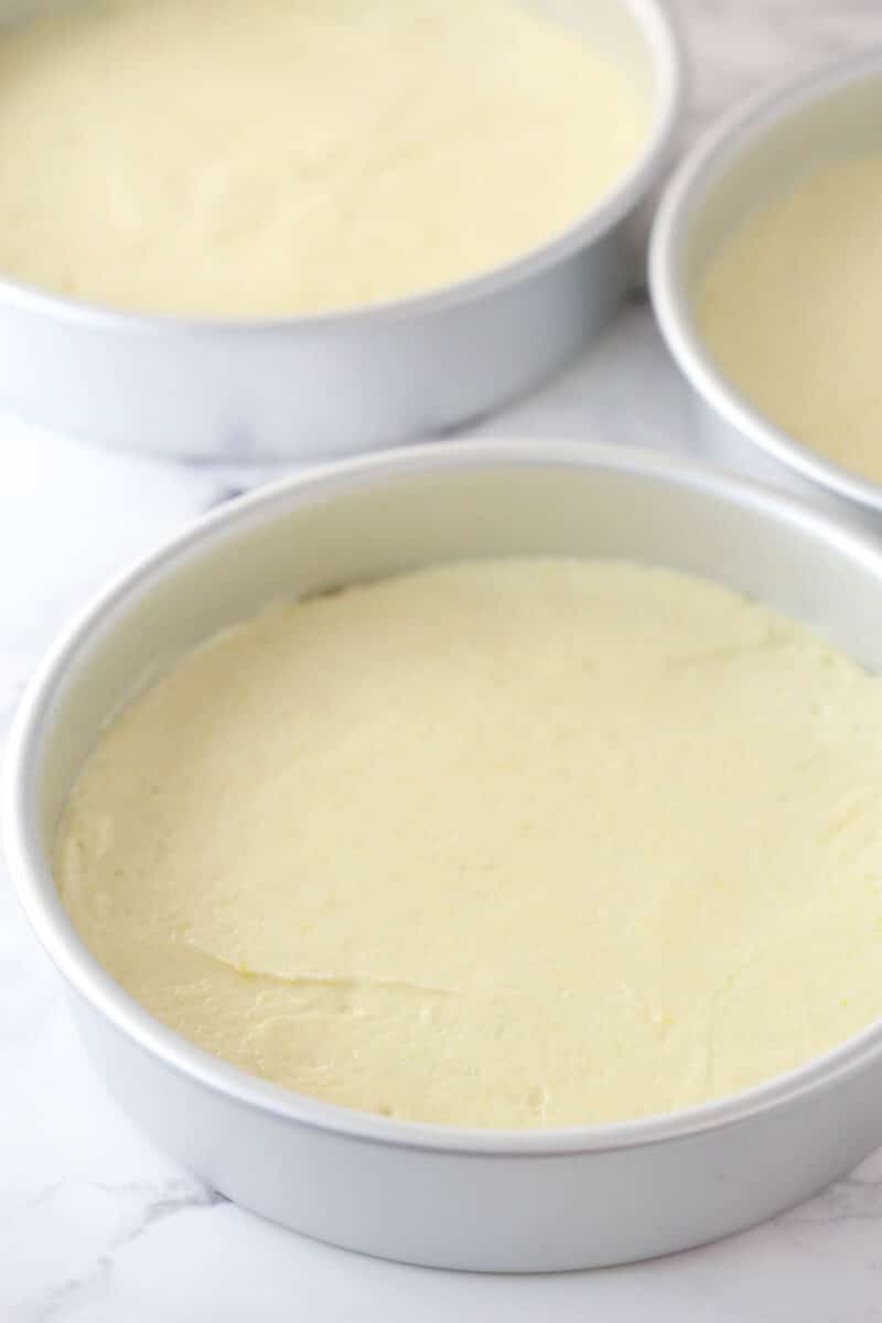 This lemon layer cake is made up of three layers of fluffy lemon cake that are filled and frosted with vibrant lemon cream cheese frosting. Lemon cake batter divided into three cake pans.
