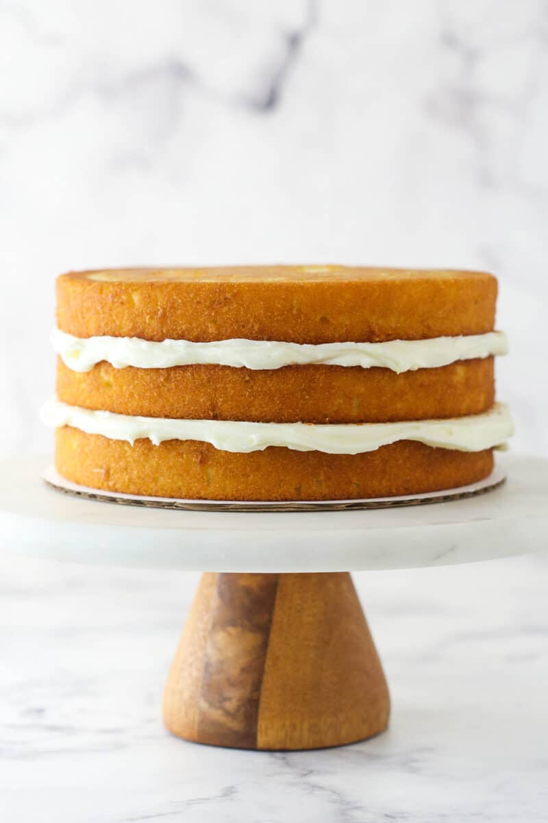 This lemon layer cake is made up of three layers of fluffy lemon cake that are filled and frosted with vibrant lemon cream cheese frosting. Three layers of lemon cake stacked on top of each other with cream cheese frosting between each layer.
