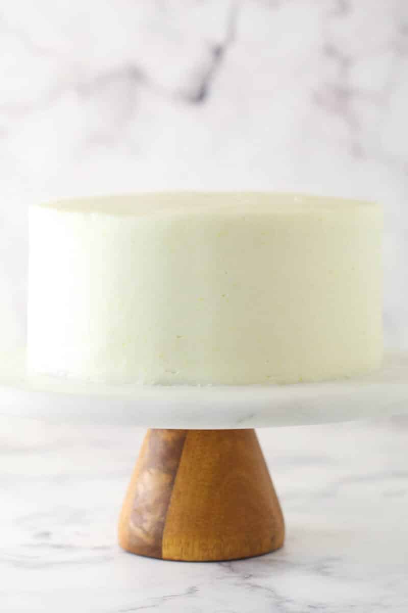 This lemon layer cake is made up of three layers of fluffy lemon cake that are filled and frosted with vibrant lemon cream cheese frosting. A smoothly frosted layer cake on a cake stand.