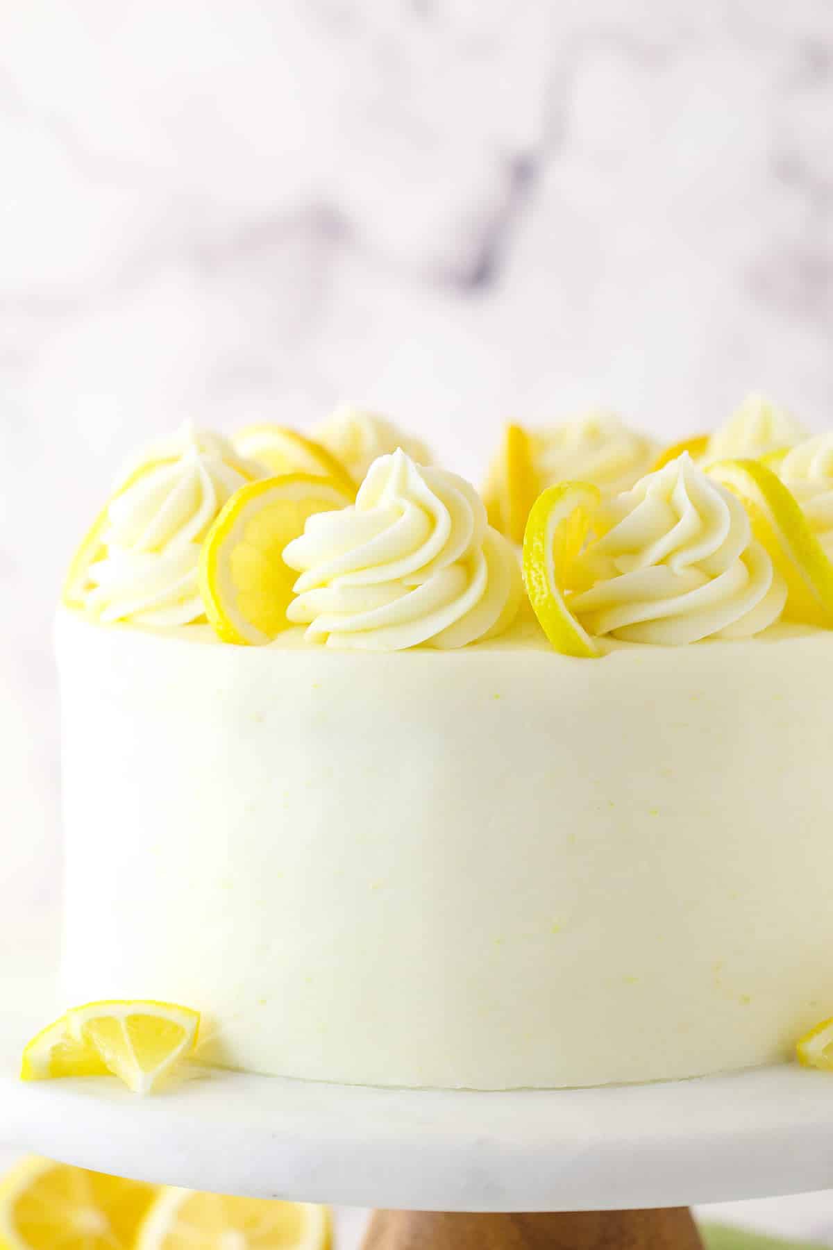 This lemon layer cake is made up of three layers of fluffy lemon cake that are filled and frosted with vibrant lemon cream cheese frosting. Lemon layer cake on a cake stand.