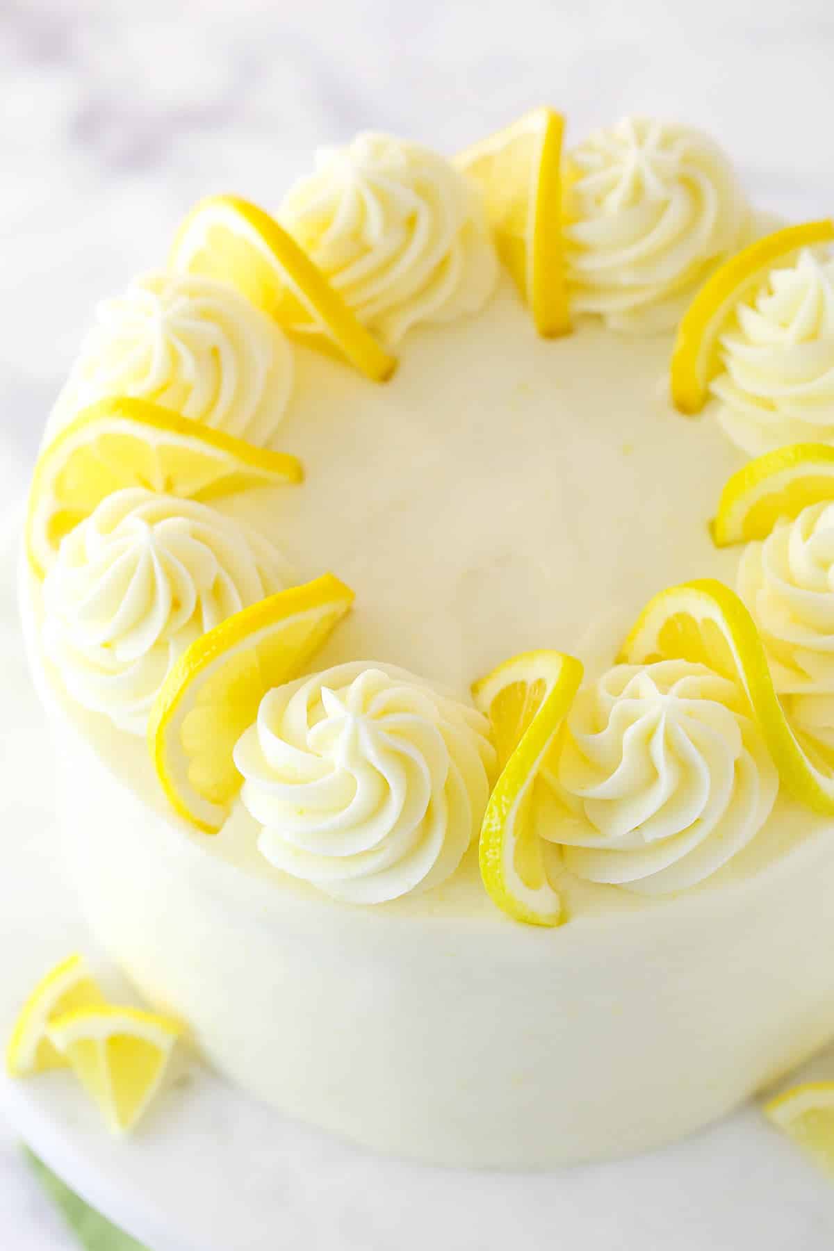This lemon layer cake is made up of three layers of fluffy lemon cake that are filled and frosted with vibrant lemon cream cheese frosting. Overhead of lemon layer cake.