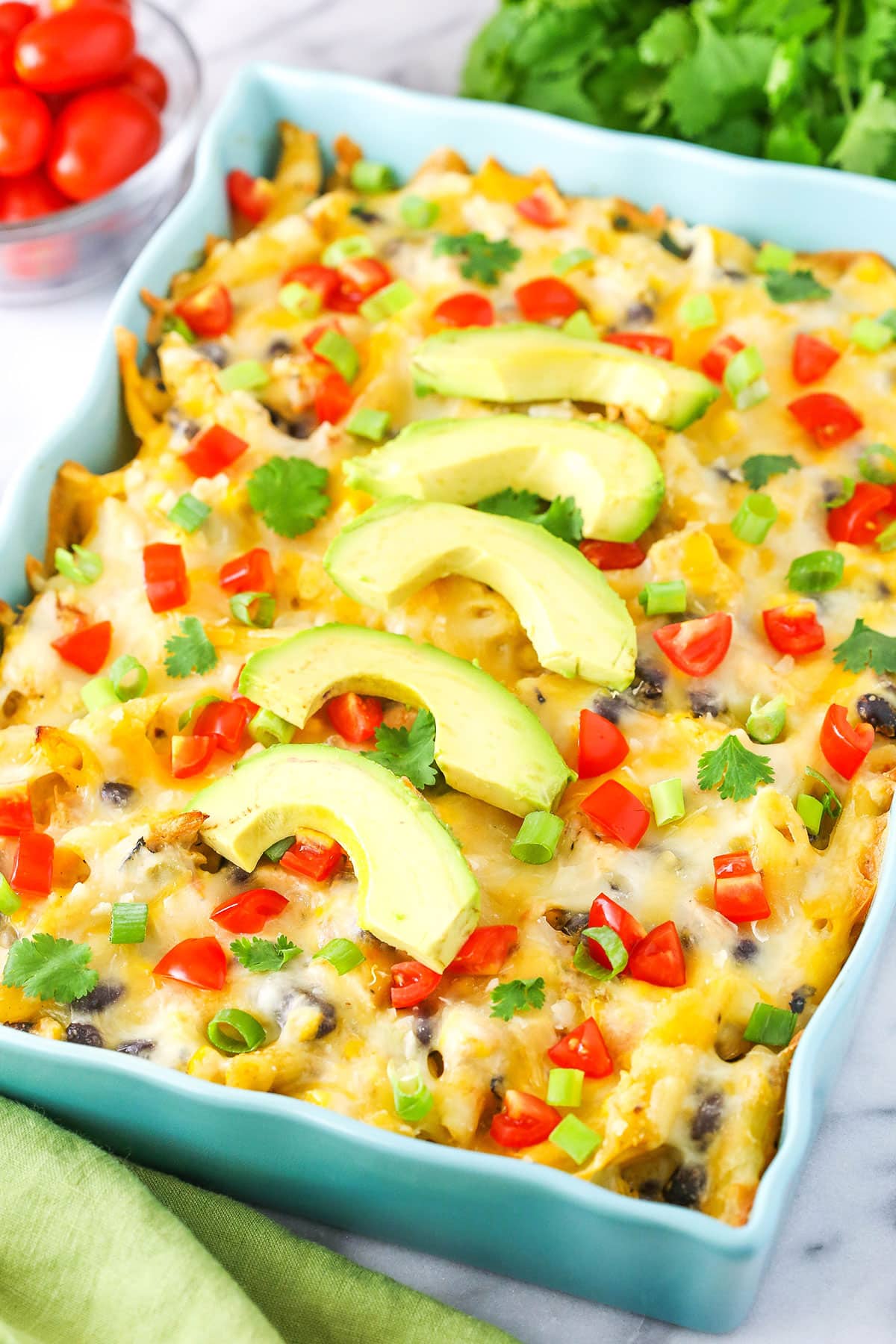This Mexican Chicken Casserole recipe is super simple to make using rotisserie chicken! Combined with penne pasta, corn, black beans, cheese, and salsa, it's a cozy chicken dinner that's perfect for any night! Mexican Chicken Casserole in a blue serving platter topped with slices of avocado