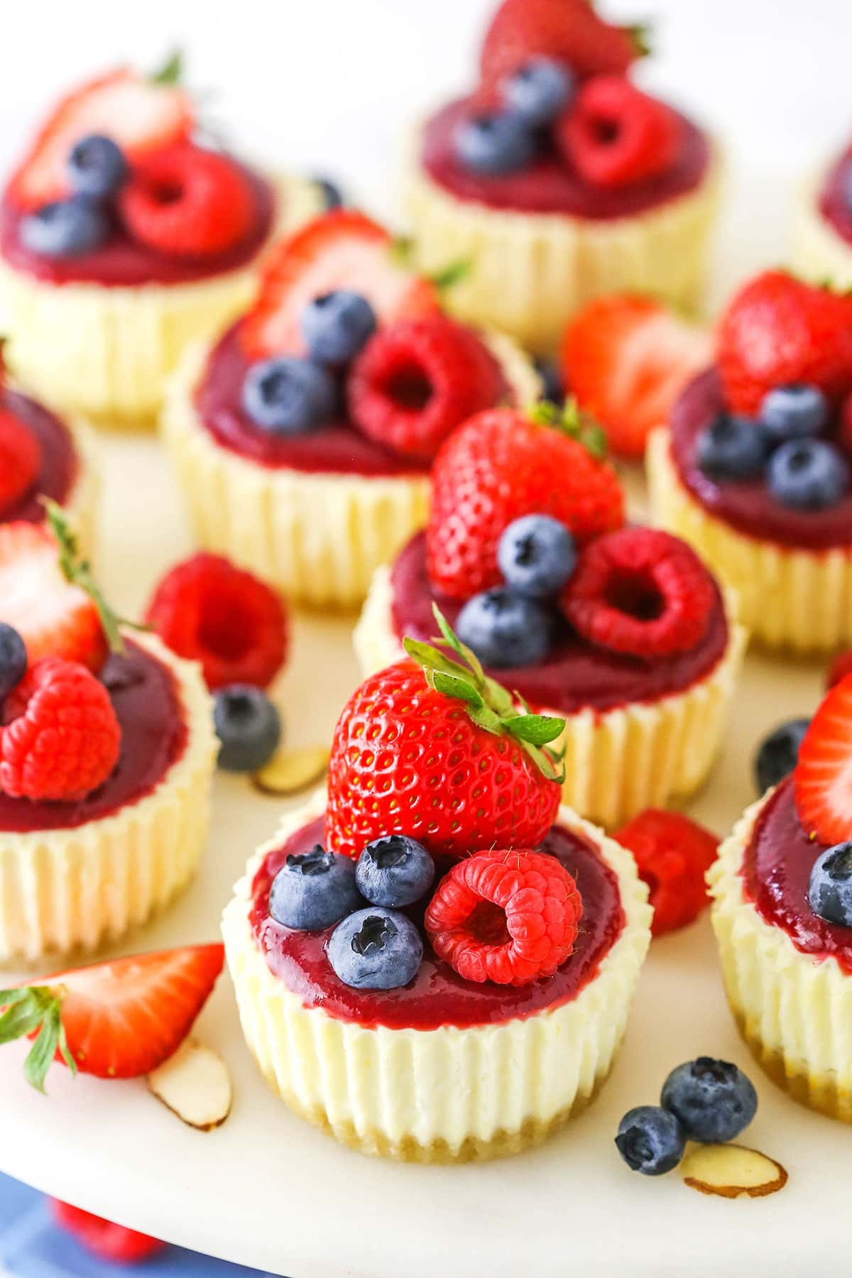 Mini Berry Almond Cheesecakes topped with strawberries, blueberries and raspberries on a white cake stand