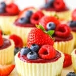 Mini Berry Almond Cheesecakes topped with strawberries, blueberries and raspberries on a white cake stand