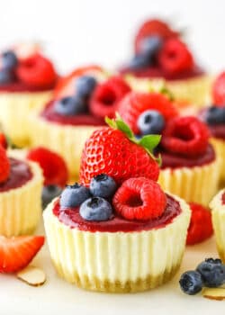 Mini Berry Almond Cheesecakes topped with strawberries, blueberries and raspberries on a white cake stand