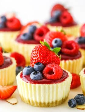 Mini Berry Almond Cheesecakes topped with strawberries, blueberries and raspberries on a white cake stand