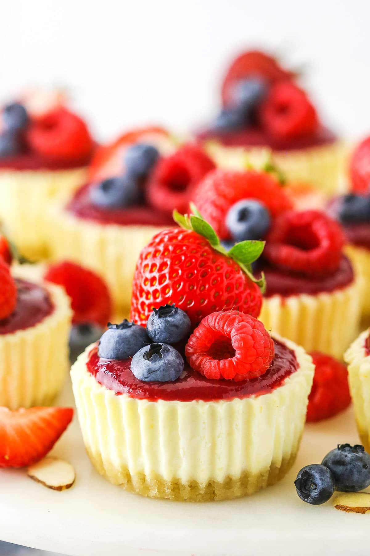 Mini Berry Almond Cheesecakes topped with strawberries, blueberries and raspberries on a white cake stand