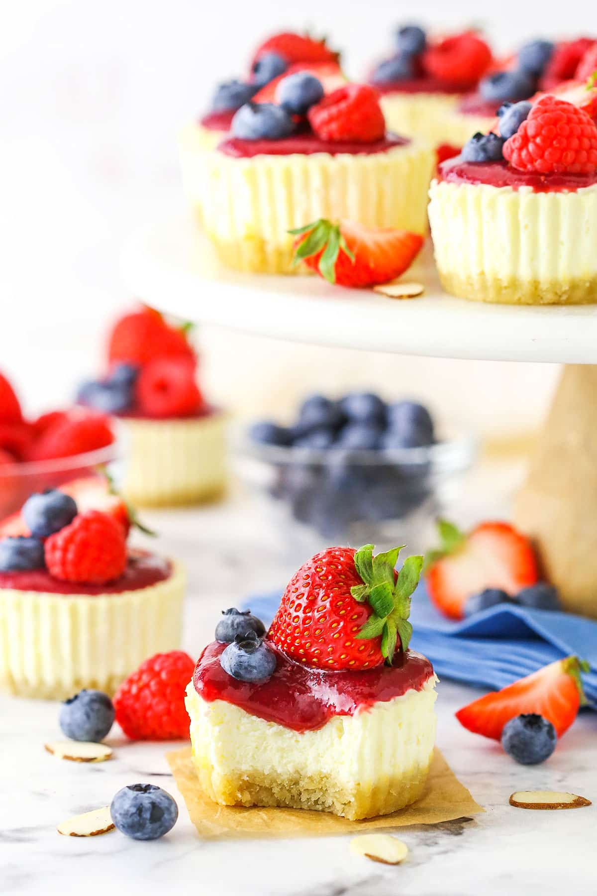 A Mini Berry Almond Cheesecake with a bite taken out on a white marble table top