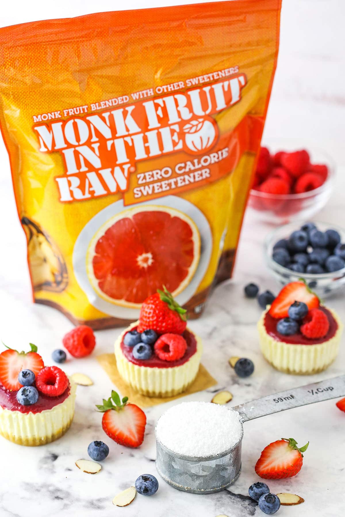 Three Mini Berry Almond Cheesecakes in front of a bag of Monk Fruit In The Raw sweetener