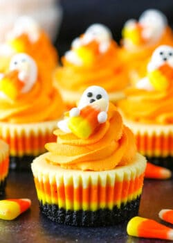 Mini Candy Corn Cheesecakes on a black table top surrounded by candy corn