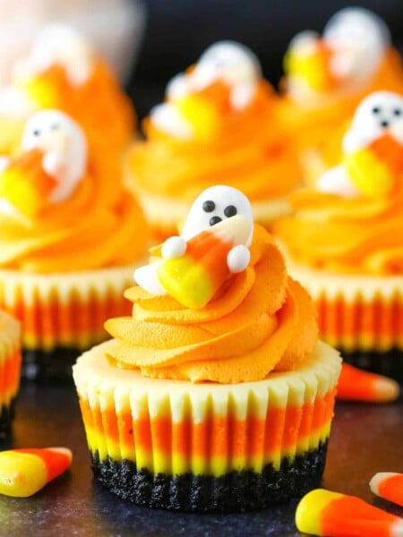 Mini Candy Corn Cheesecakes on a black table top surrounded by candy corn
