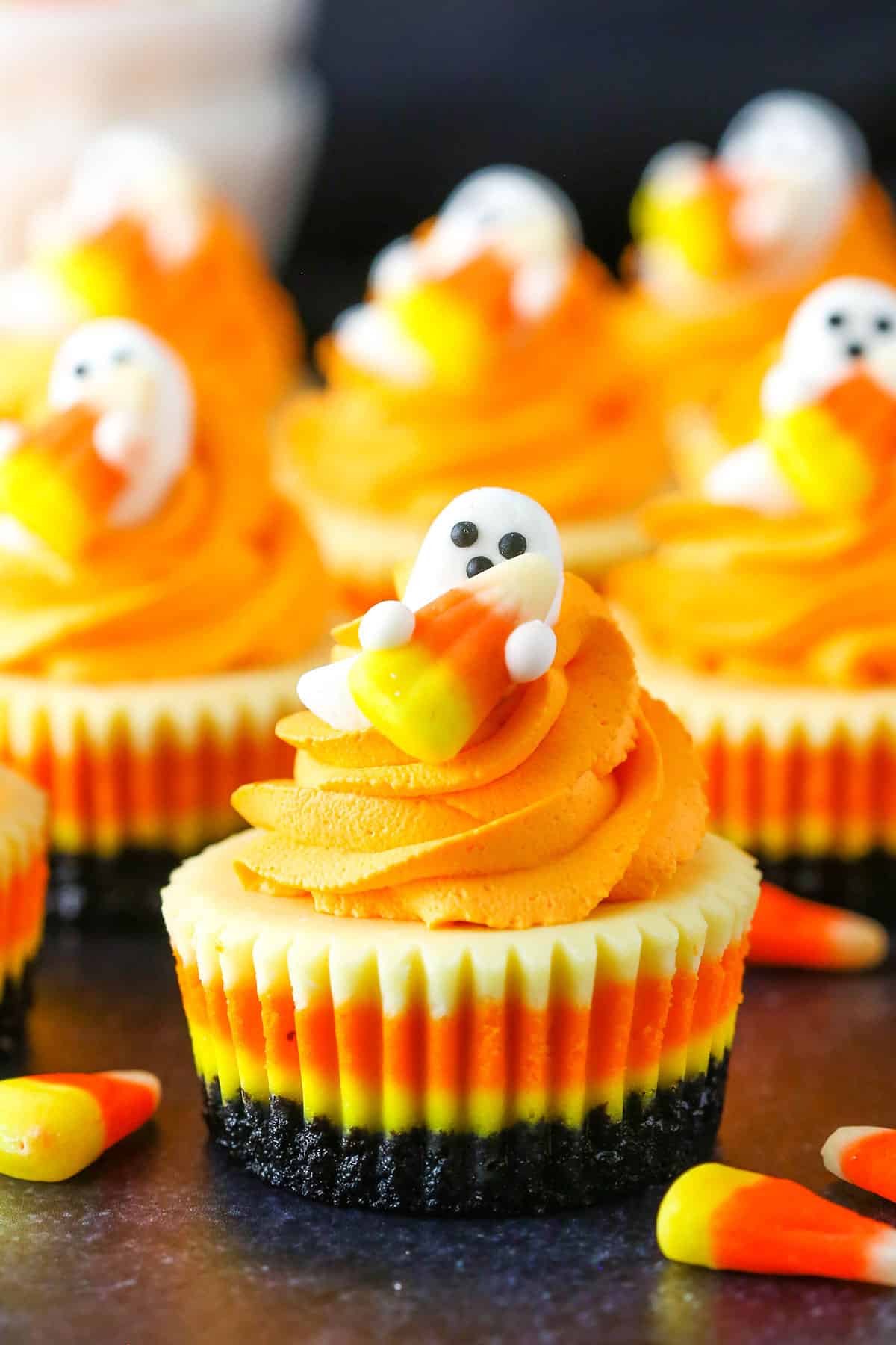 Mini Candy Corn Cheesecakes on a black table top surrounded by candy corn