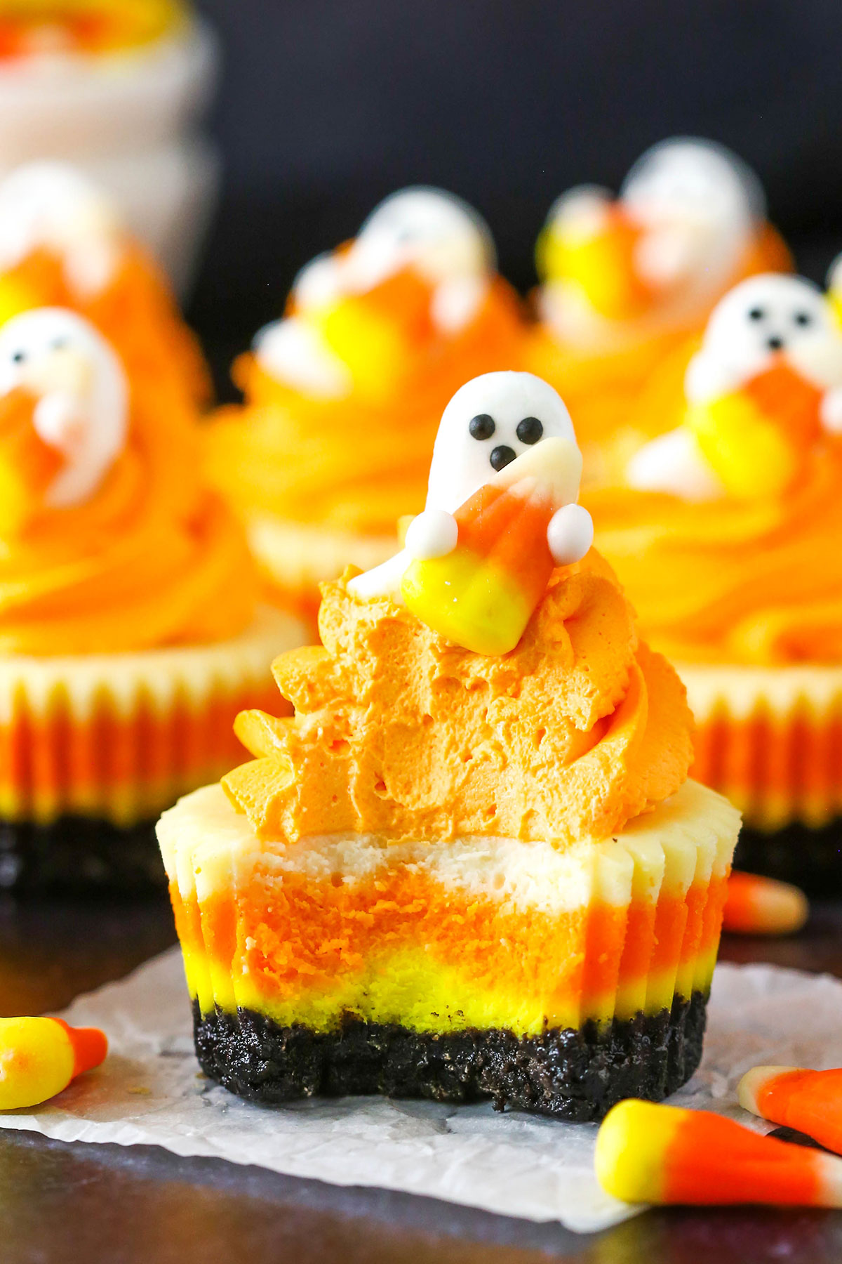 These Mini Candy Corn Cheesecakes are easy to make and such a fun Halloween dessert! If you're looking for Halloween party food ideas, these are perfect for sharing. A Mini Candy Corn Cheesecake with a bite removed on a black table top surrounded by candy corn