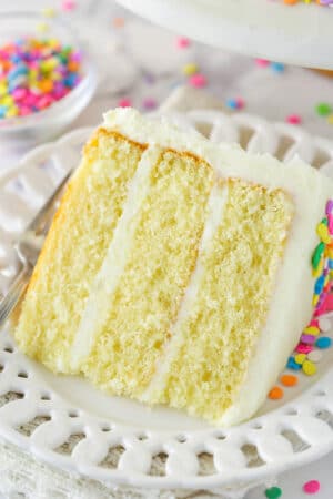 A slice of moist vanilla layer cake on a plate with a fork.