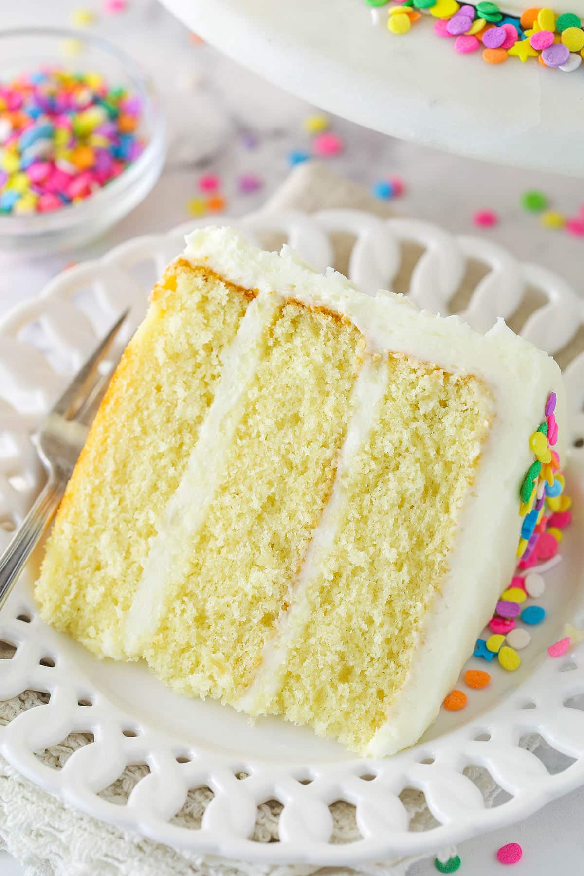 A slice of moist vanilla layer cake on a plate with a fork.