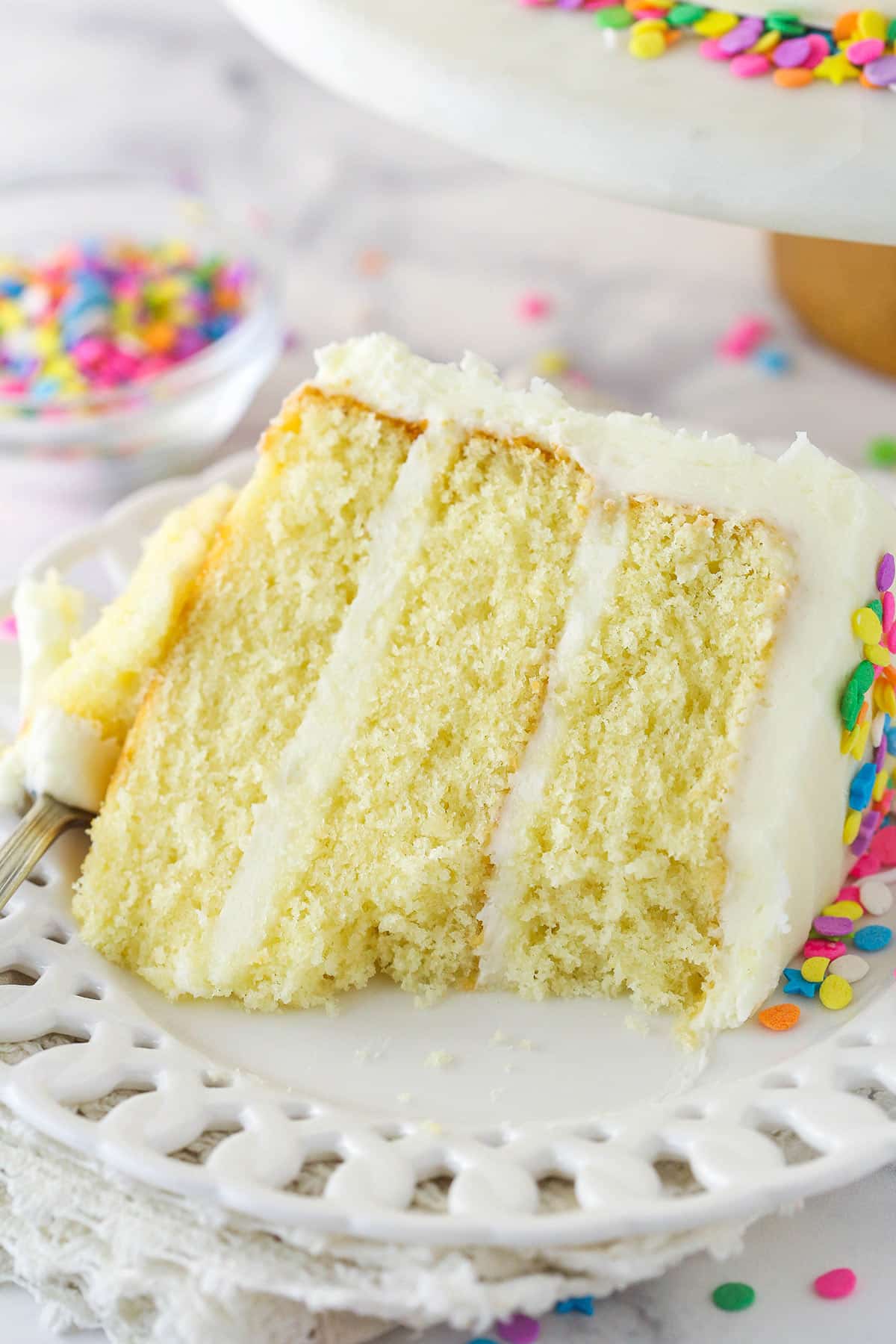 A slice of moist vanilla layer cake on a plate with a bite taken out of it.