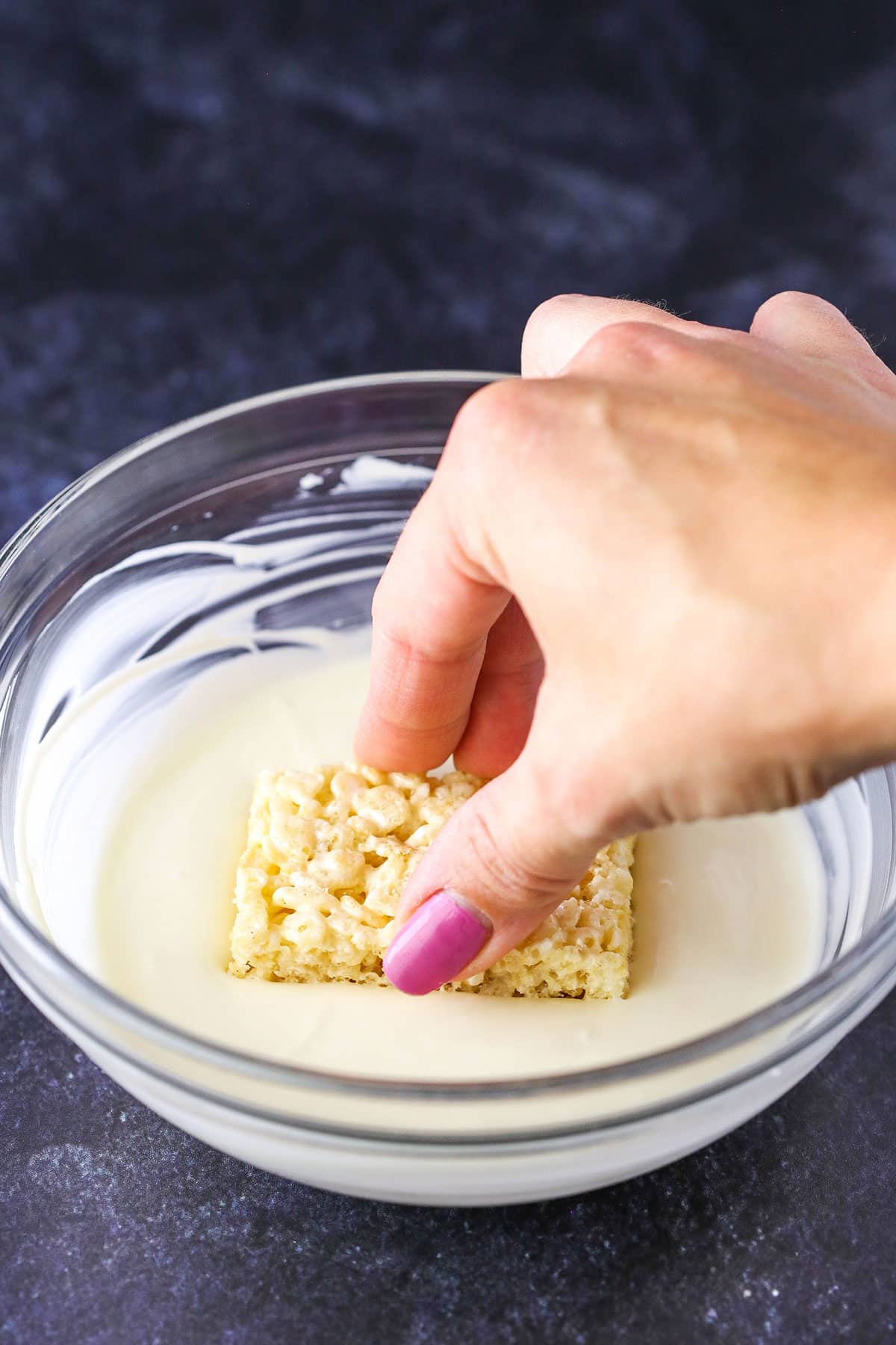 A step in making Mummy Rice Krispies Treats showing dipping a Rice Krispies Treat into melted white chocolate