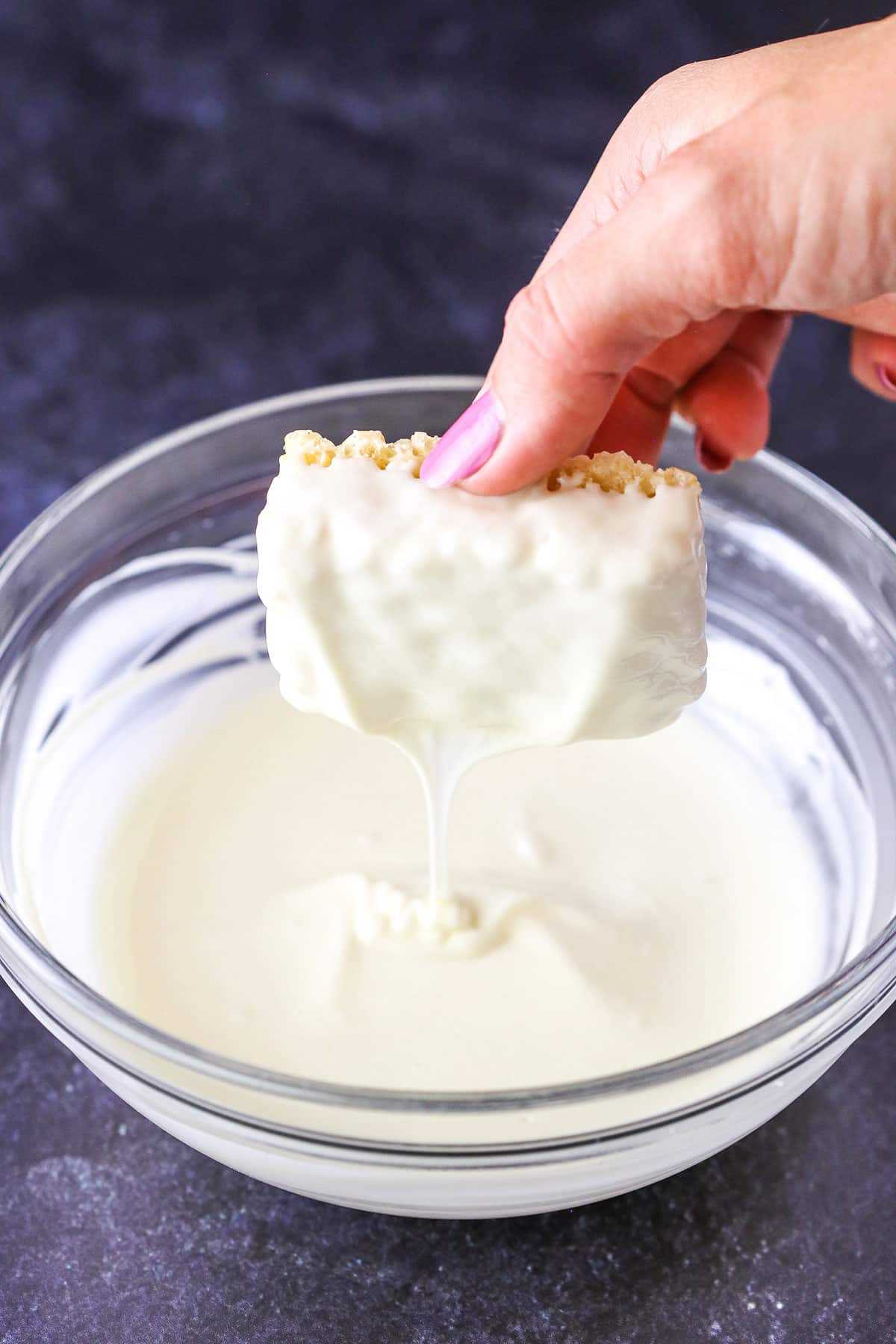 A step in making Mummy Rice Krispies Treats showing the back and sides covered with white chocolate and shaking off any excess.