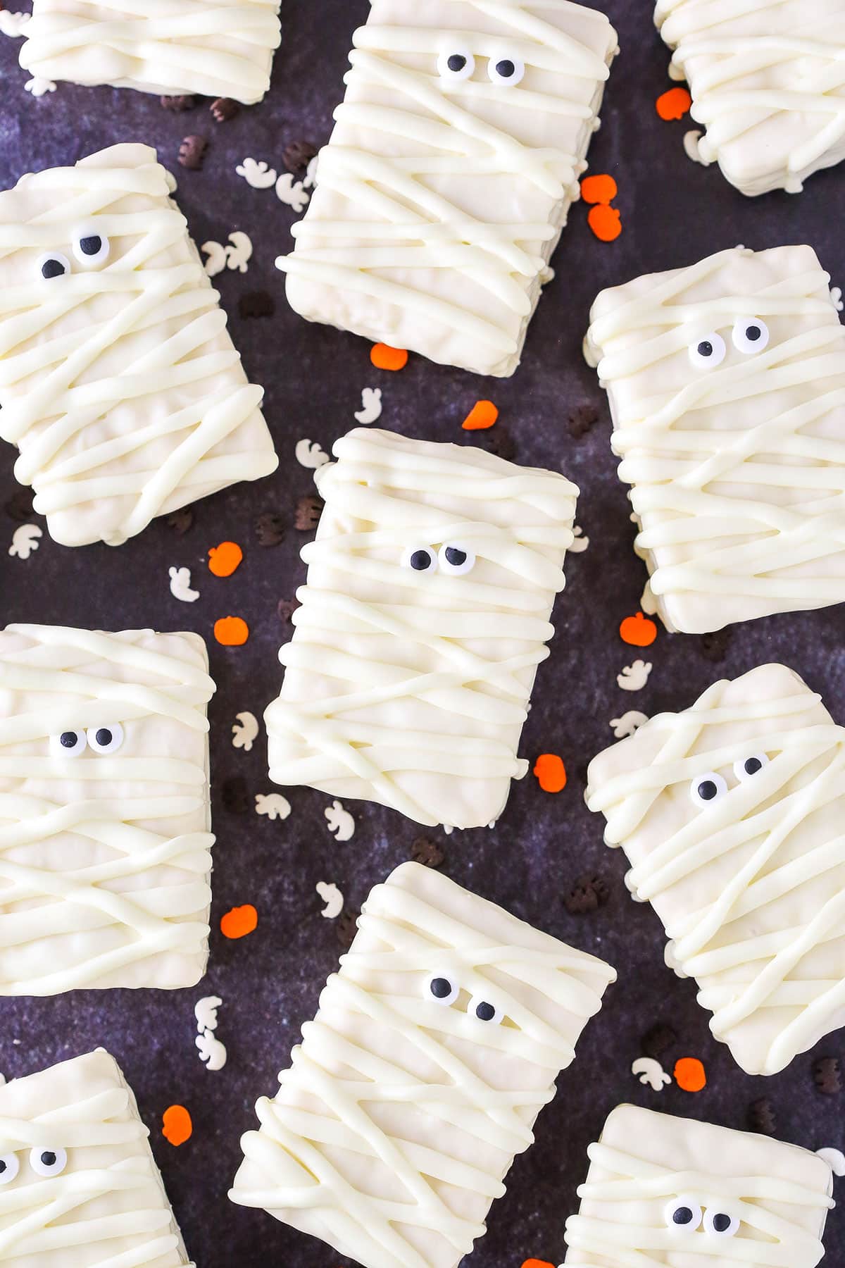 Overhead view of Mummy Rice Krispies Treats on a black table top surrounded by orange and white Halloween sprinkles