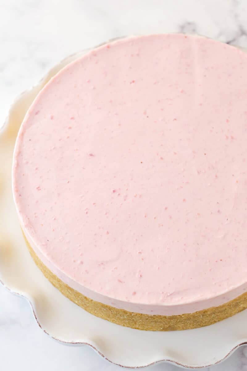 Undecorated no bake strawberry cheesecake on a serving platter.