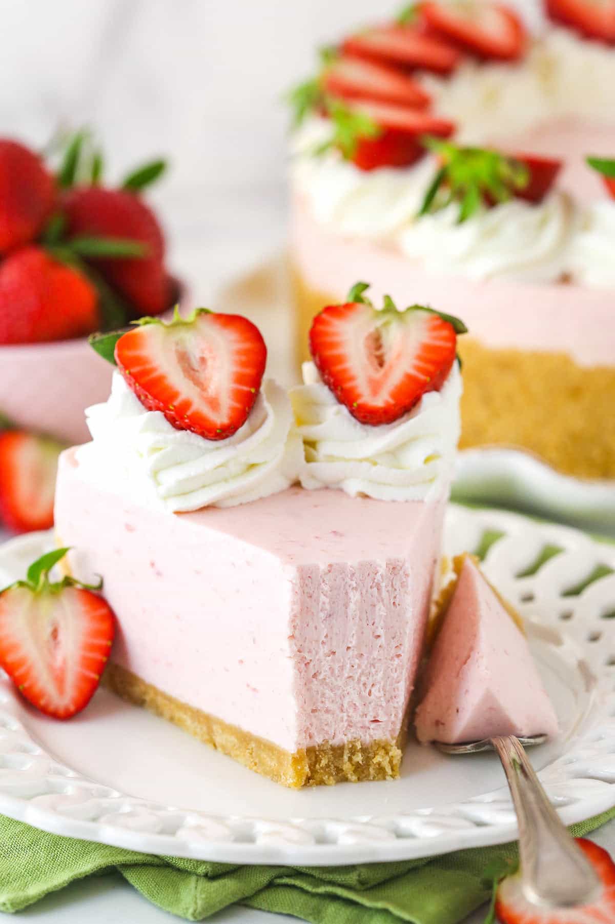 A slice of no bake strawberry cheesecake on a plate with a fork taking a bite out of it.