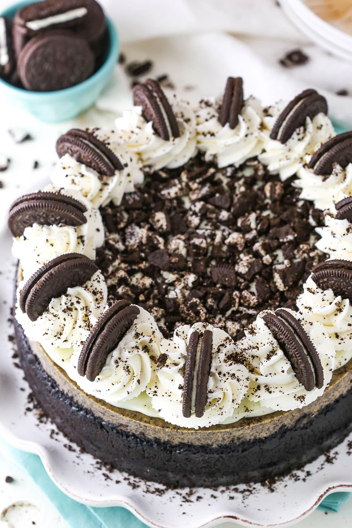 Overhead view of an Oreo Cheesecake on a white cake stand on top of a blue cloth