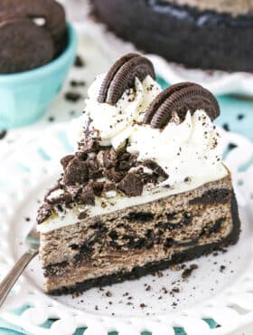 A slice of Oreo Cheesecake next to a fork on a white plate