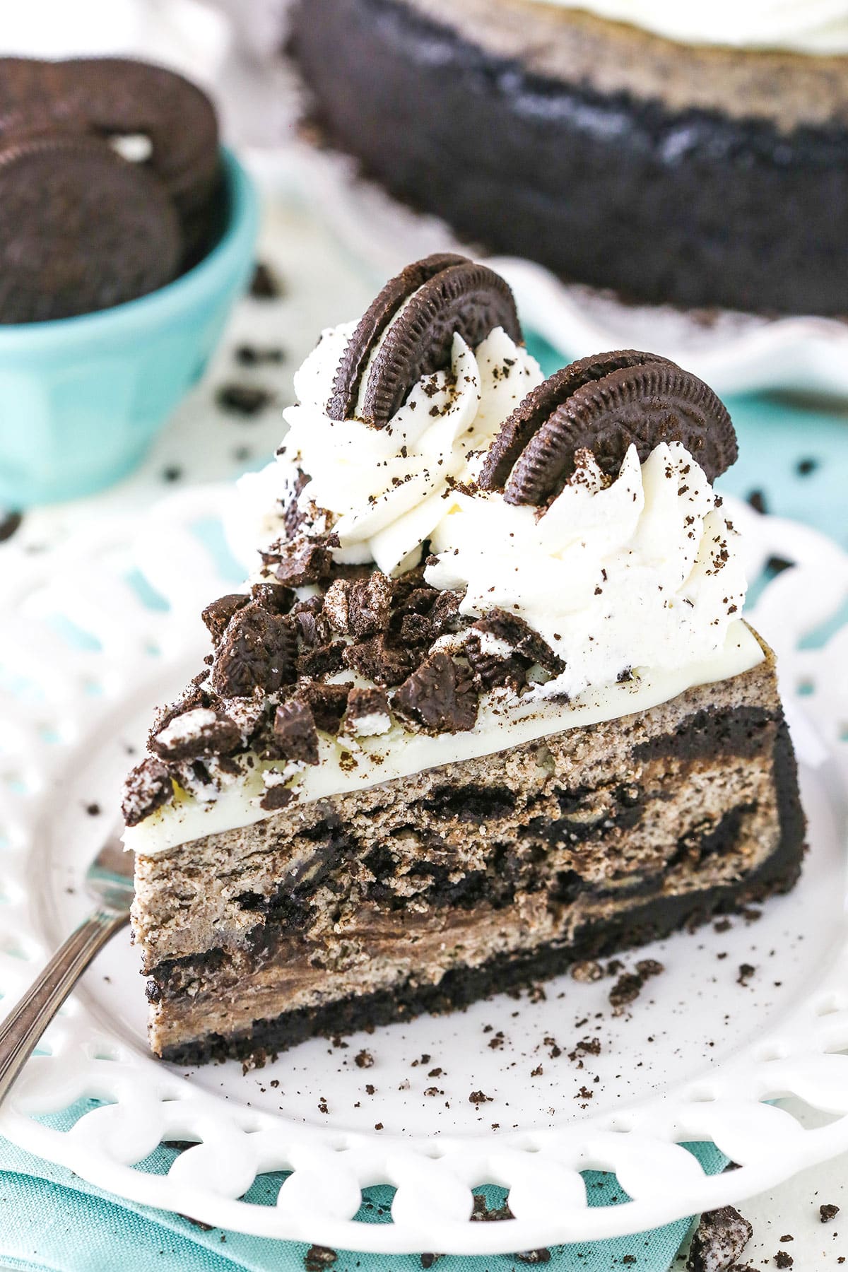 A slice of Oreo Cheesecake next to a fork on a white plate