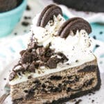 A slice of Oreo Cheesecake next to a fork on a white plate