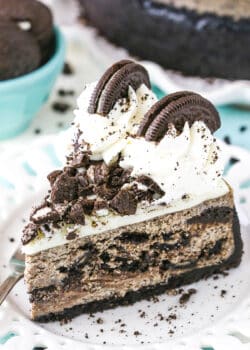 A slice of Oreo Cheesecake next to a fork on a white plate