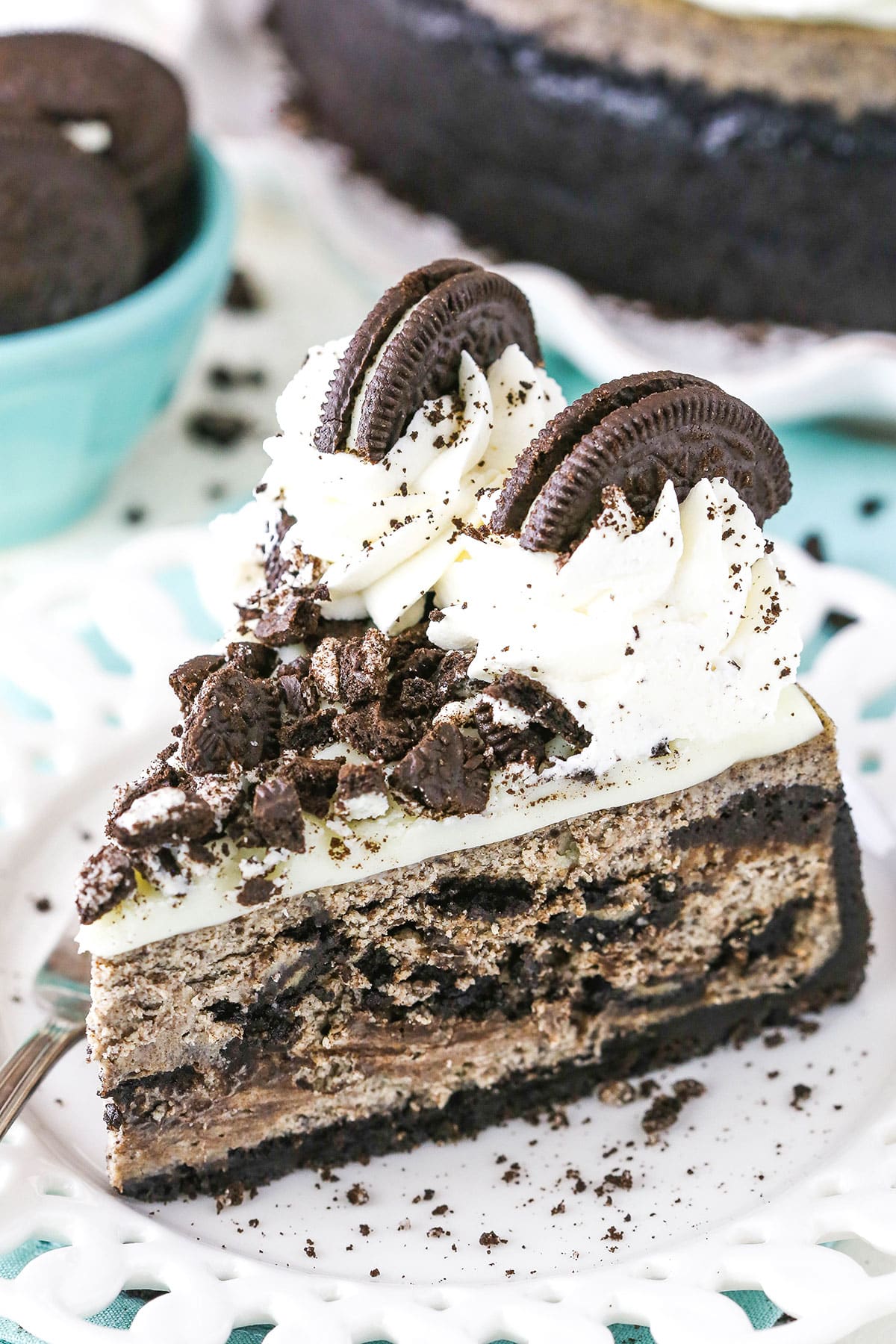 A slice of Oreo Cheesecake next to a fork on a white plate