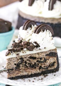 A slice of Oreo Cheesecake next to a fork on a white plate