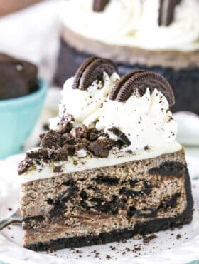 A slice of Oreo Cheesecake next to a fork on a white plate