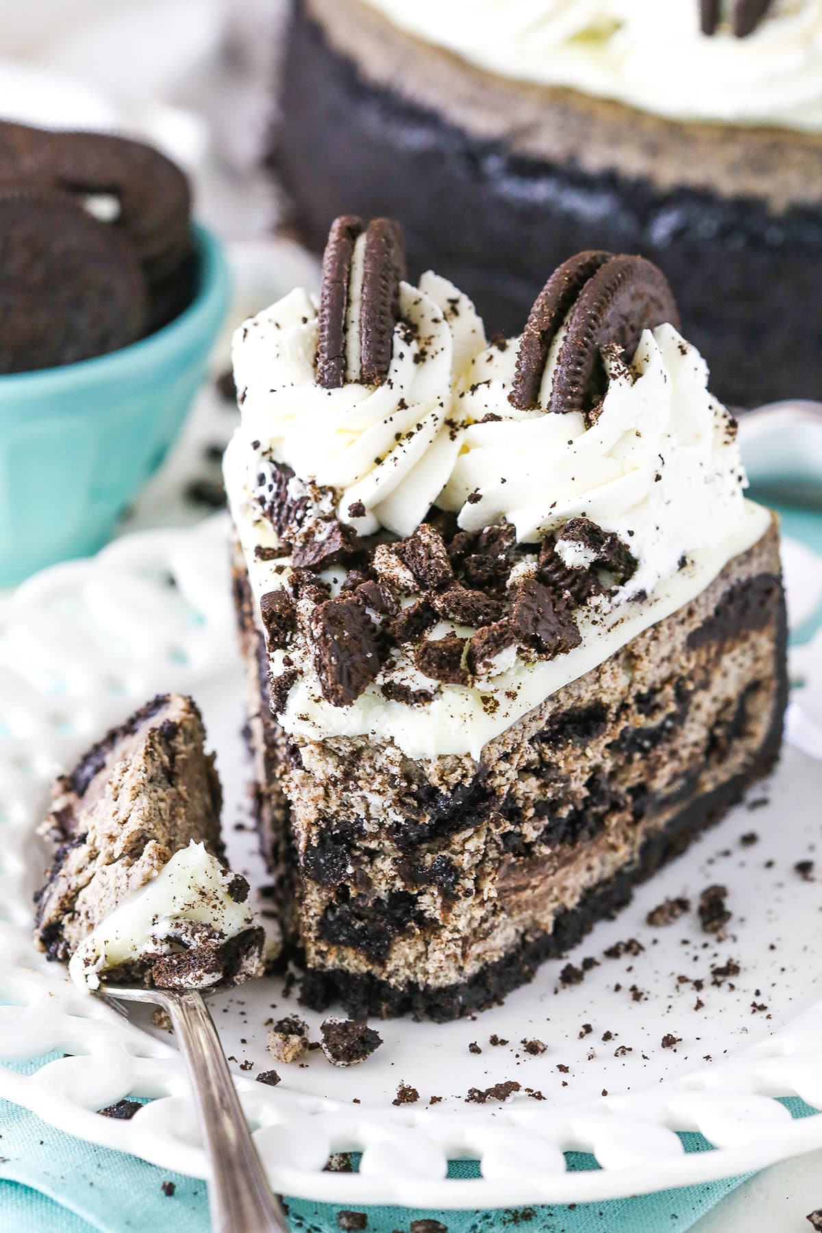 A slice of Oreo Cheesecake with a bite removed next to a fork on a white plate