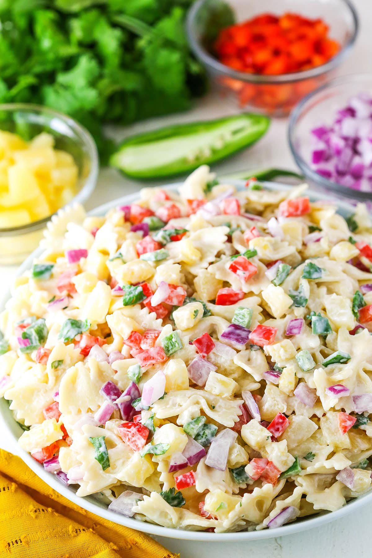 This Pineapple Salsa Pasta Salad is such a light and delicious pasta salad for summer! Made with the best flavors of pineapple salsa - pineapple, lime juice, cilantro, red pepper, red onion and jalapeños - it's full of my favorite flavors! Pineapple Salsa Pasta Salad in a white bowl on a white table
