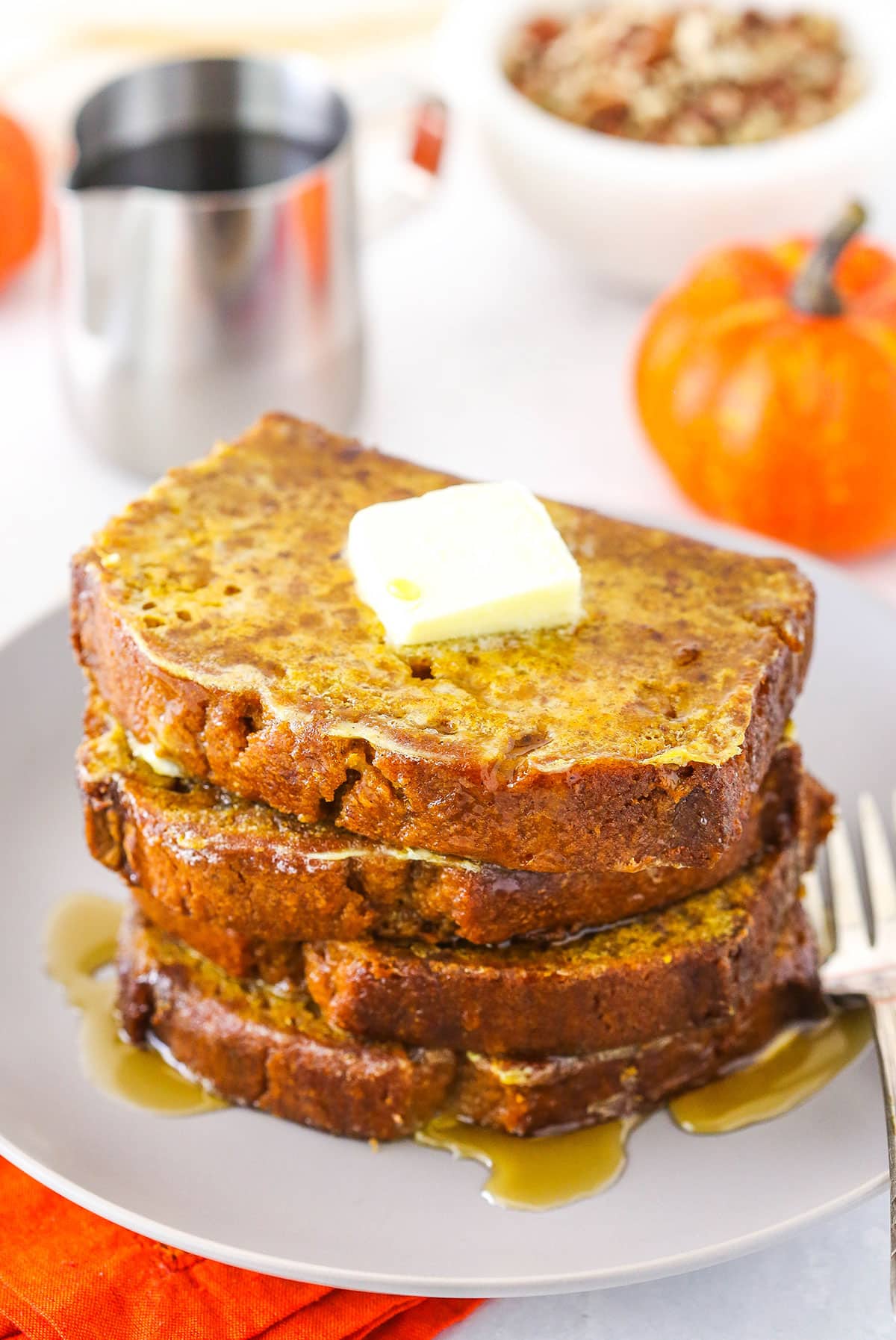 Four slices of Pumpkin Bread French Toast stacked on a white plate and topped with syrup and butter