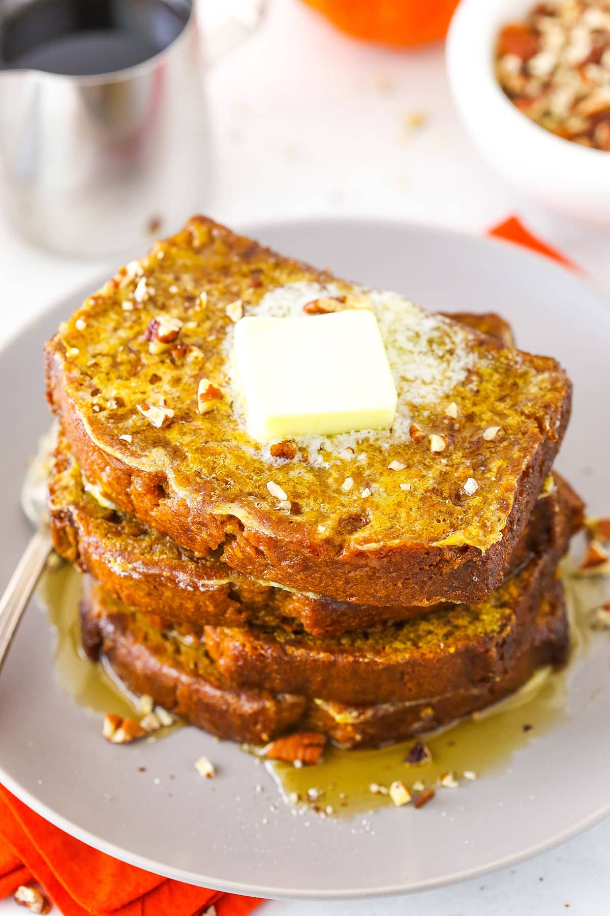 Four slices of Pumpkin Bread French Toast stacked on a white plate and topped with syrup and butter