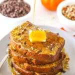 Syrup being poured over four slices of Pumpkin Bread French Toast stacked on a white plate