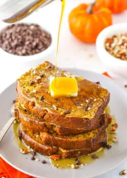 Syrup being poured over four slices of Pumpkin Bread French Toast stacked on a white plate