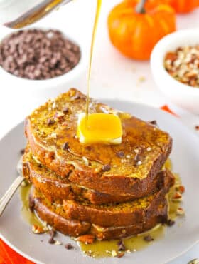Syrup being poured over four slices of Pumpkin Bread French Toast stacked on a white plate