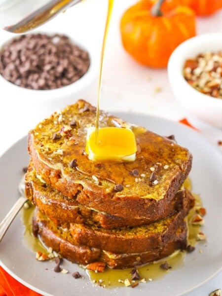 Syrup being poured over four slices of Pumpkin Bread French Toast stacked on a white plate