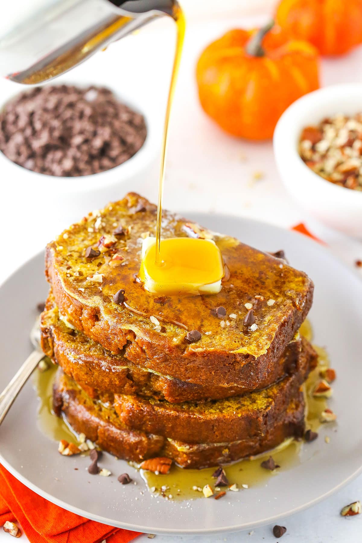 Syrup being poured over four slices of Pumpkin Bread French Toast stacked on a white plate