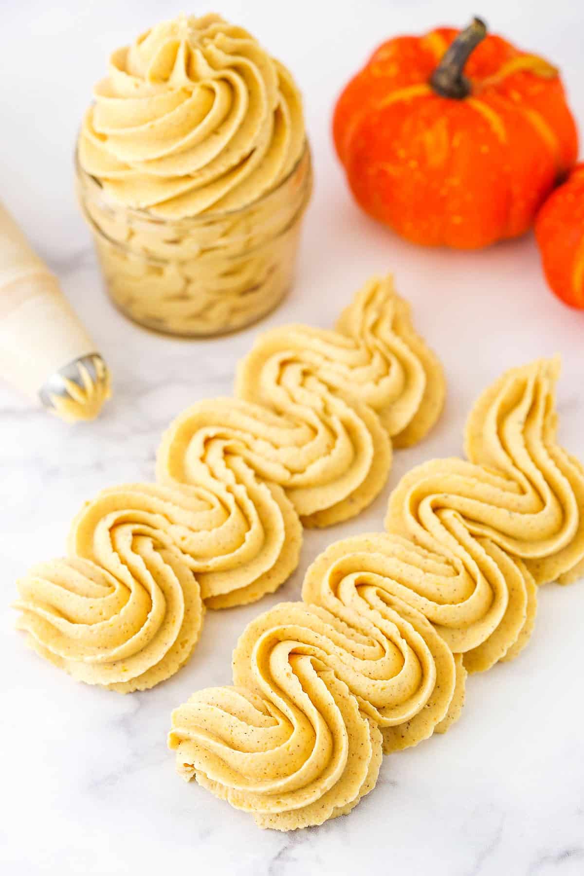 This easy Pumpkin Spice Buttercream Frosting is perfect for Fall! It's flavored with pumpkin and lots of spice and great for frosting cakes, cupcakes, cookies and more! Pumpkin Spice Buttercream Frosting piped onto a white marble countertop