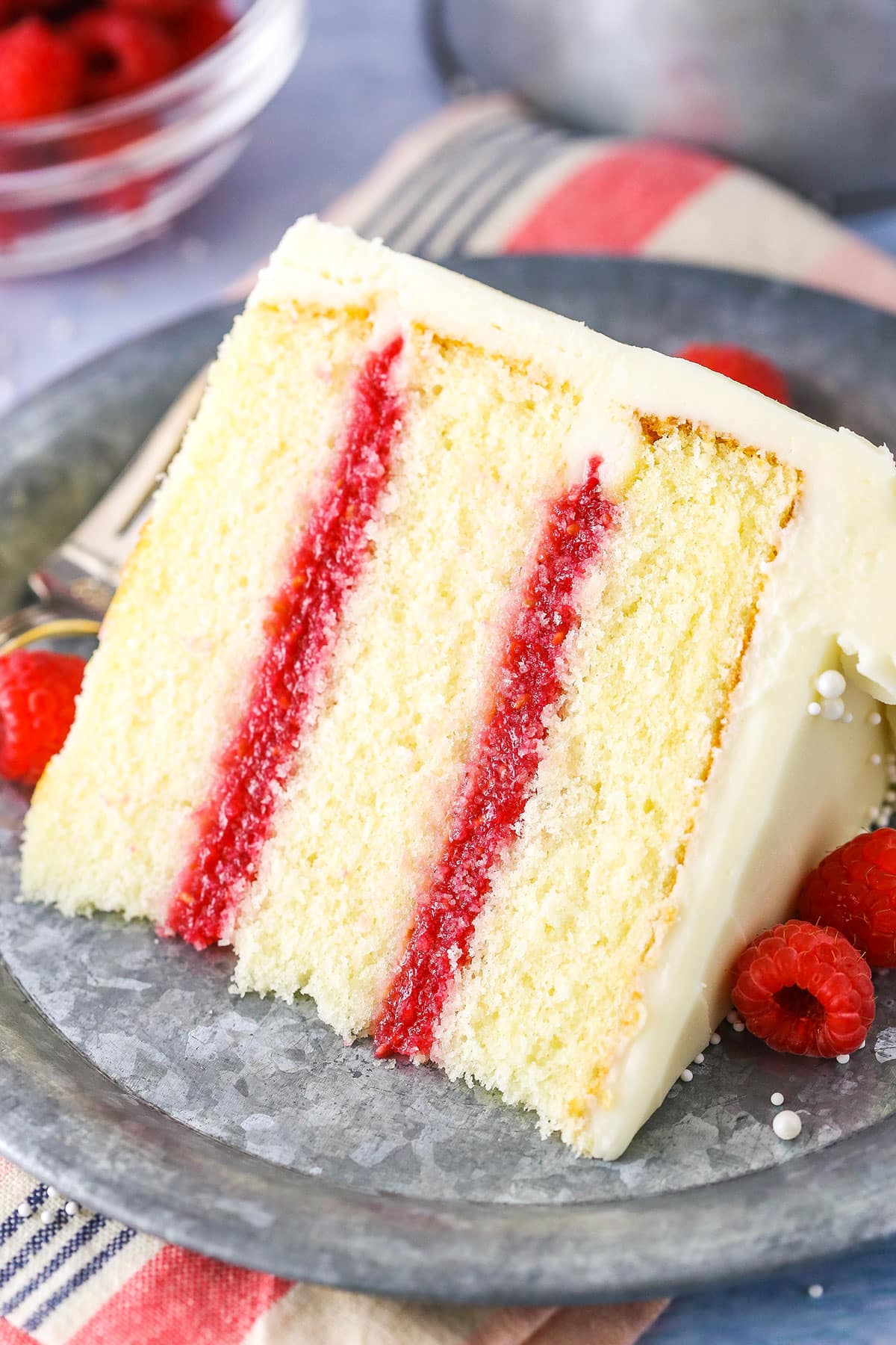 A slice of Raspberry Dream Cake on it's side next to a fork on a grey plate