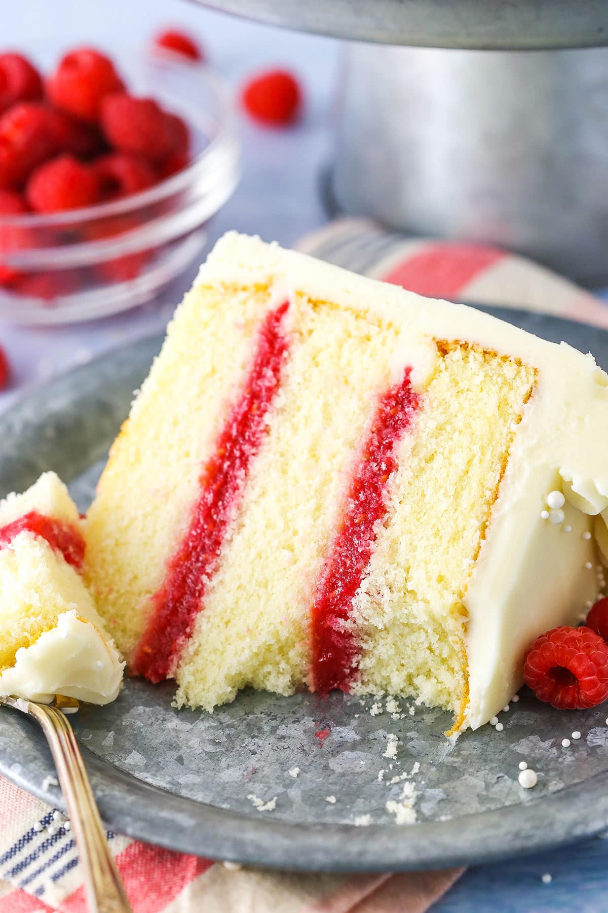 A slice of Raspberry Dream Cake with a bite removed on it's side next to a fork on a grey plate