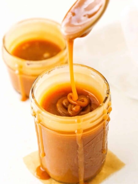 Overhead of dripping Salted Caramel Sauce off a spoon into a clear glass jar