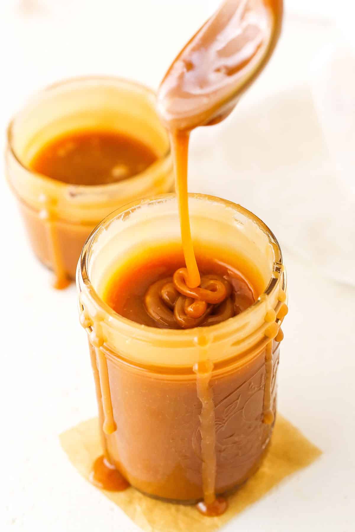 Overhead of dripping Salted Caramel Sauce off a spoon into a clear glass jar