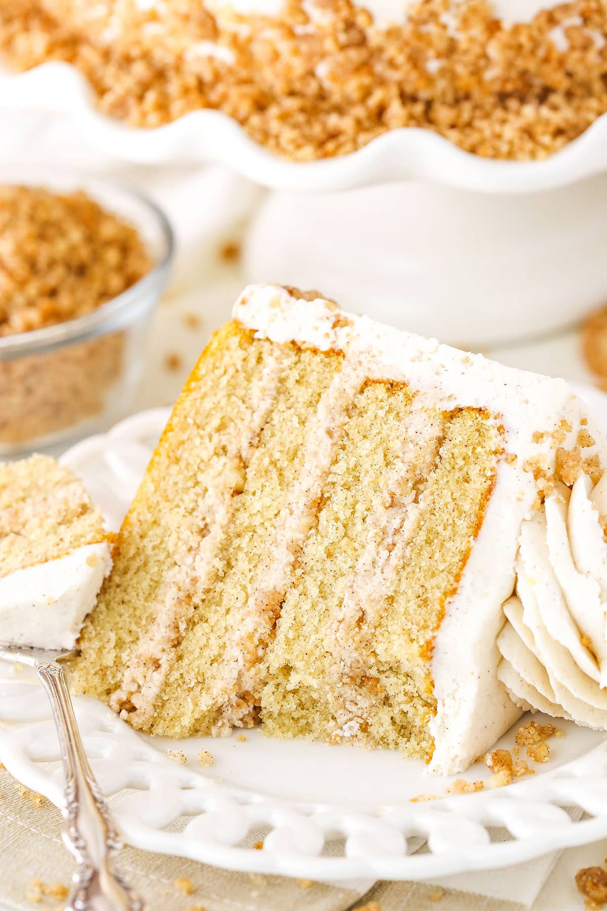 A slice of Snickerdoodle Layer Cake on it's side with a bite removed next to a fork on a white plate